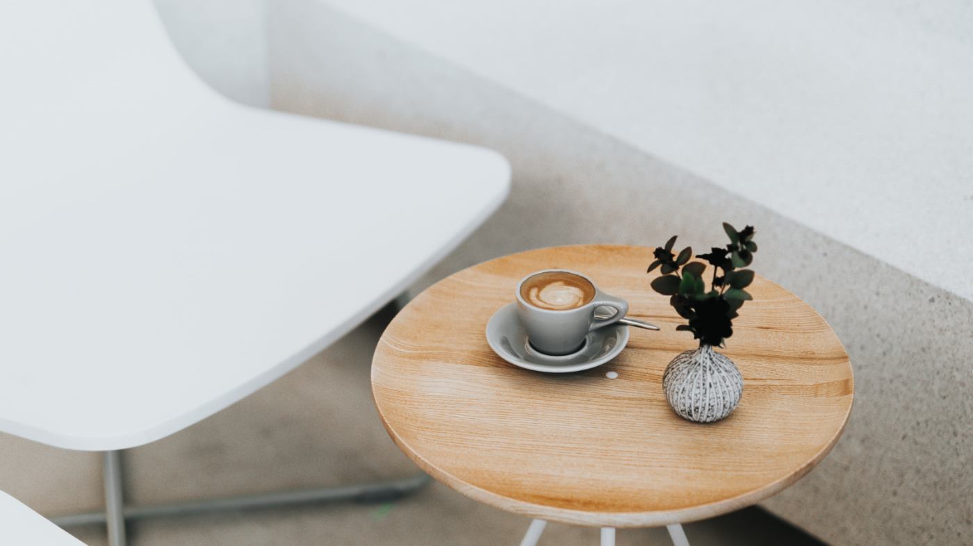 A cappuccino and a plant are placed on a small coffee table.